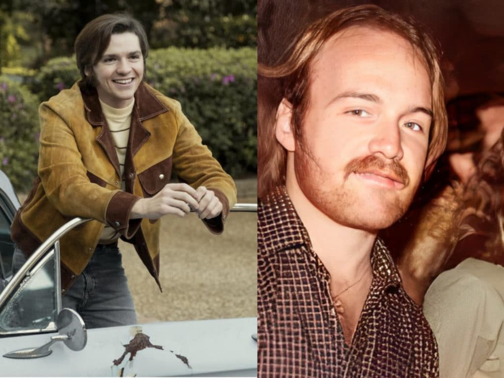 Two men with long brown hair, one is wearing a brown jacket and leaning on a old car door and smiling. The other man has a brown mustache and is looking forward, while wearing a brown short open at the collar. 